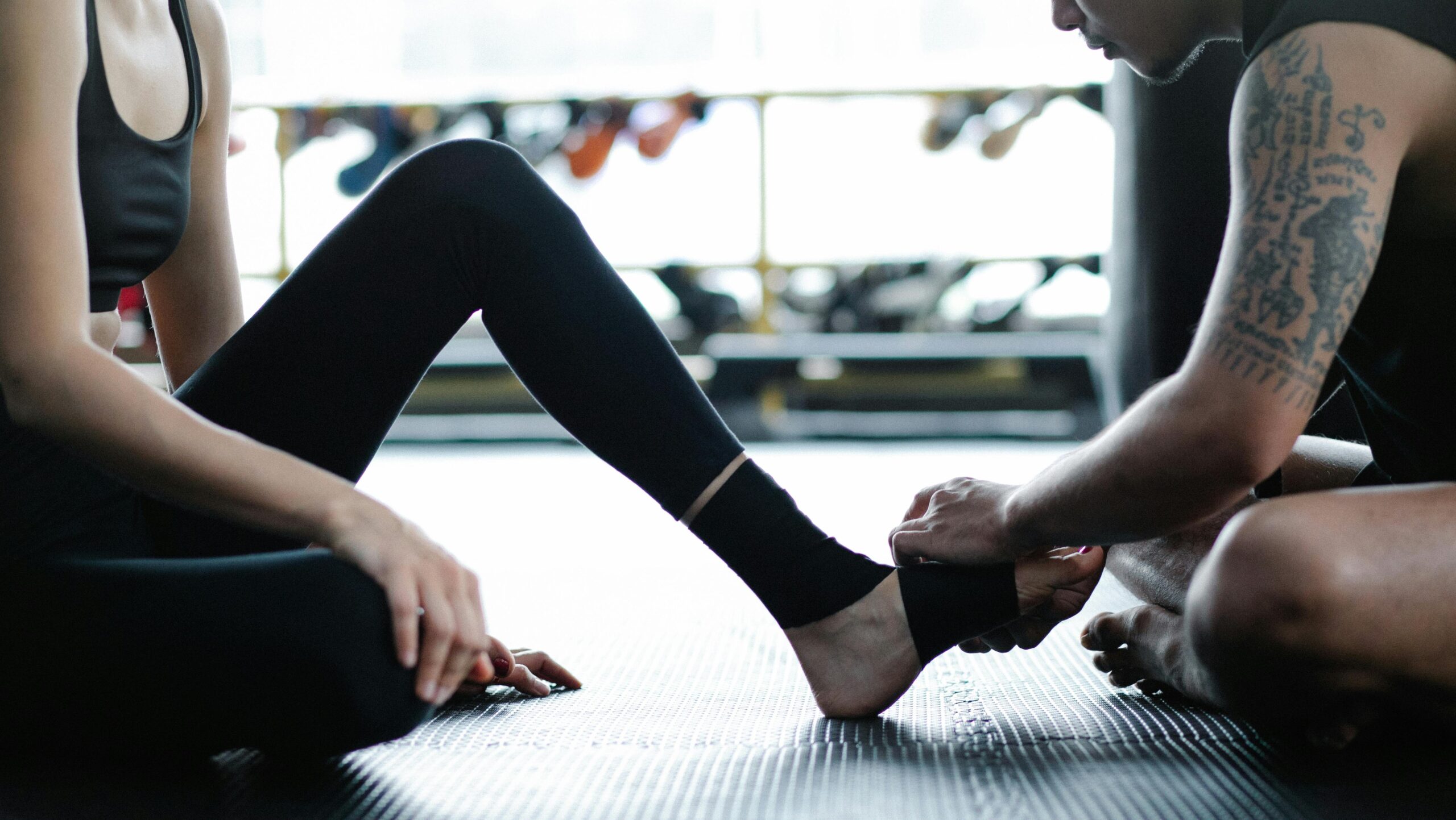 Two adults in gym attire preparing for a fitness session by wrapping an ankle.